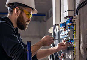 A male electrician works in a switchboard with an electrical connecting cable. A male electrician works in a switchboard with an electrical connecting cable.
