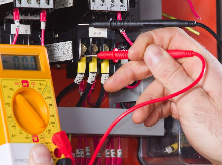 A person's hand holding an electrical meter to gauge an electrical system. Complete Electrical, Commercial, and HVAC Maintenance Plans.